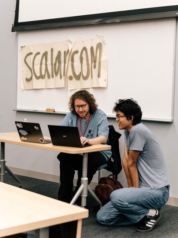 Two hackers demoing their project beside a hand-lettered sign